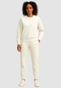 Felpa bianca e pantaloni della tuta abbinati realizzati in tessuto morbido, con polsini a costine e un piccolo logo sul petto e sulla coscia.