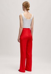 Rode wijde broek van een gestructureerde stof, met een hoge taille en elastische band, gecombineerd met een witte mouwloze top.