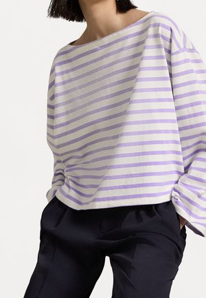 Wzorzysty bawełniany sweter z szerokim dekoltem, w naprzemienne jasnofioletowe i białe paski, zestawiony z ciemnymi spodniami.