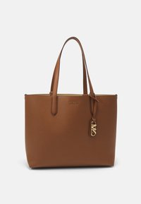 Hnědá kožená taška přes rameno s texturovaným povrchem, dvojitými uchy a akcentem loga ze zlaceného kovu. Otevřený vršek s prostorným interiérem.