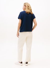 T-shirt blu navy a maniche corte con dettagli in button sulle spalle, abbinato a pantaloni bianchi a gamba dritta e sneakers bianche, visto da dietro.