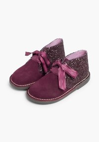 Botas de tobillo de ante púrpura con una parte superior brillante, lazos de cinta de satén y forro rosa en contraste. Detalles cosidos a lo largo de la suela.