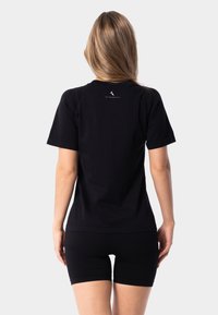 Sort bomulds t-shirt med korte ærmer, der har et diskret logo på ryggen. Sammen med sorte shorts i samme materiale.