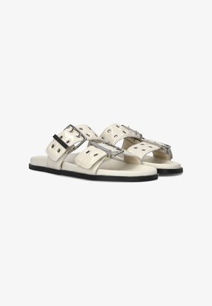 Witte leren sandalen met twee brede banden voorzien van zilveren gespen en oogjes, flatte zwarte zolen en een minimalistisch ontwerp.