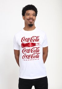Bílý bavlněný tričko s červeným logem Coca-Cola v kurzívě a ilustrací láhve. Krátké rukávy a klasický kulatý výstřih.