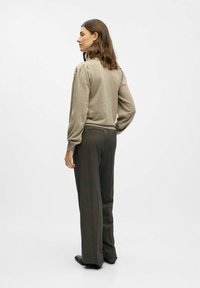 Beige Sweater mit langen Ärmeln und Schulterdetails, kombiniert mit dunklen, weiten Hosen und schwarzen Schuhen, von hinten betrachtet.