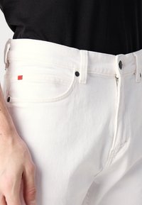 Witte denim jeans met een rechte pasvorm, voorzien van een ritssluiting, twee voorke pocketen en een klein rood merklabel op de linkerzak.