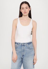 Valge singelkaelusega tank top, mis on valmistatud siledast kangast, koos kerge sinise kõrge vöökohaga teksapükstega, kus on klassikaline viie tasku disain.