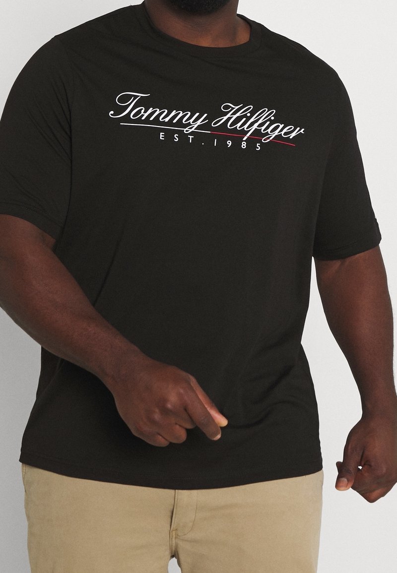 Černé bavlněné tričko s bílým a červeným logem "Tommy Hilfiger" s kurzívním písmem, krátkými rukávy a kulatým výstřihem.