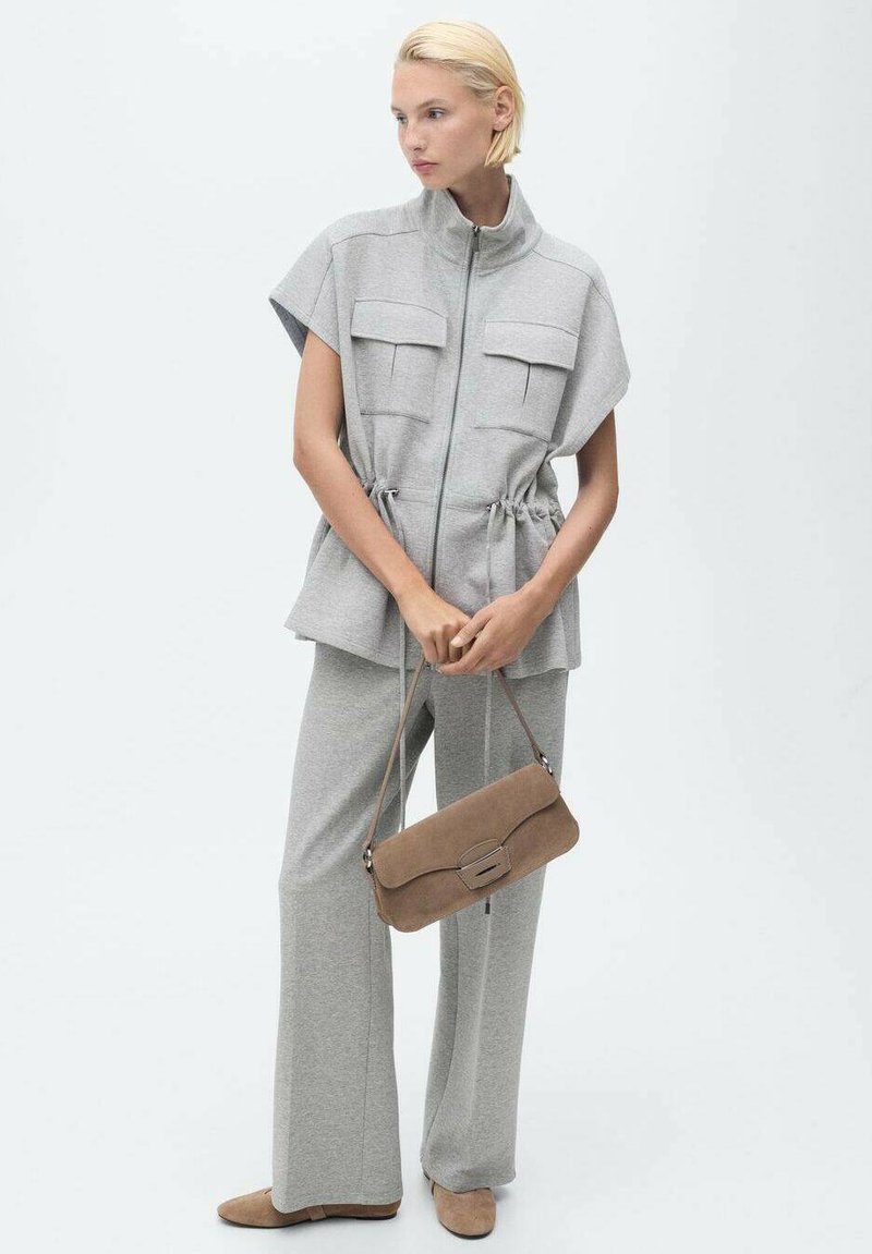 Veste grise à manches courtes avec deux poches poitrine et taille à cordon, associée à un pantalon ample assorti et un sac à main taupe.