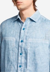Camicia button-up azzurro chiaro in tessuto testurizzato, con colletto aperto, due tasche sul petto e bottoni turchesi a contrasto.