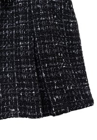 Il tessuto tweed in bianco e nero presenta una trama testurizzata con un motivo a quadri. I bordi sono rifiniti in modo ordinato, evidenziando i dettagli della cucitura.