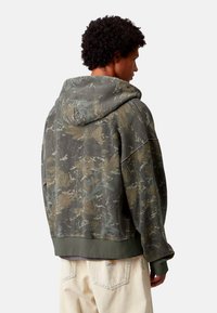 Sudadera de gran tamaño con patrón de camuflaje en verde apagado, marrón y gris. Tejido suave con capucha ajustable y dobladillo y puños acanalados.