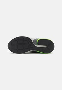 Sport shoe sole featuring a textured black rubber with a green accent, a wide, rounded shape, and structured grip patterns for traction.