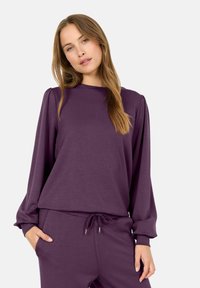 Conjunto de ropa de casa morado que incluye una camiseta de manga larga con cuello redondo y corte holgado, acompañada de pantalones con cintura elástica. Textura de tejido suave.