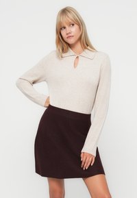 Vaalea beige pitkähihainen paita, jossa on kaulus ja avainaukko-yksityiskohta, yhdistetty tumman burgundin minihameen kanssa. Pehmeä tekstuuri, tiukka muotoilu ja rento tyyli.