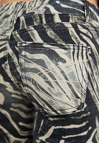 Jeans de mezclilla con estampado de cebra en negro y crema, que presentan un diseño de bolsillo distintivo y una tela texturizada con detalles de costura en contraste.