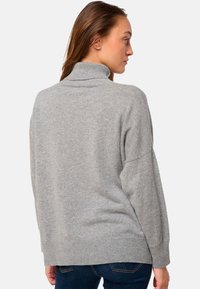Pull à col roulé gris avec une coupe décontractée, texture douce, ourlet côtelé et épaules tombantes. Le dos présente un design minimaliste.