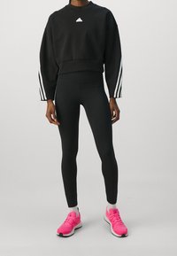 Felpa nera corta con logo bianco, leggings neri e scarpe da ginnastica rosa acceso. Presenta strisce bianche verticali sulle maniche.