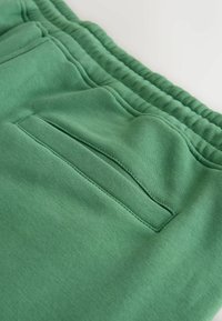 Pantalon de jogging en tissu doux vert avec une taille élastique et une poche fendue horizontale à l'arrière.