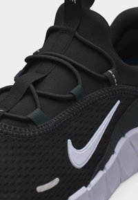 Μαύρο αθλητικό παπούτσι Nike με λευκό λογότυπο swoosh, μαύρα ελαστικά κορδόνια και λευκή σόλα με τμήματα, σε κοντινό πλάνο.