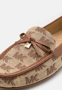 Mocassin en cuir marron avec une toile à motif tan comportant le logo répété "MK", complété par un nœud et un détail en métal doré.