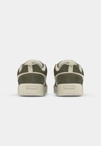 Olive green suede sneakers with cream accents, featuring a structured design, thick sole, and prominent "PUMA" branding on the heel.