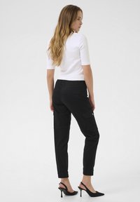 Pantalons cargo noirs avec poches latérales, chevilles resserrées et texture lisse, associés à un haut blanc ajusté et des talons ouverts noirs.