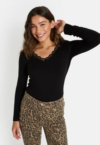 Bodysuit noir à manches longues avec encolure en V ornée de dentelle, associé à un pantalon à taille haute imprimé léopard.