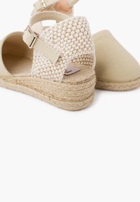 Beeži espadrillid kudumisega pealmise osa, reguleeritava pahkluu rihmaga ja looduslikust jute-st tallaga. Sile kanvasest varbaosa ja tekstureeritud kand detail.