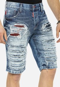 Denim-Shorts in verblasstem Blau mit abgenutzten Stellen und fransigen Kanten. Fünf-Taschen-Design mit rotem Stichakzent an der Vorderseite.