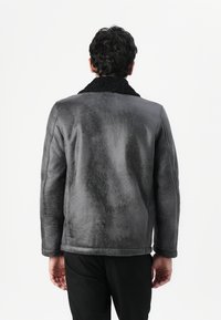 Giacca shearling grigia con colletto in pelliccia nera. Finitura liscia, maniche lunghe e vestibilità leggermente ampia. Design semplice senza decorazioni.