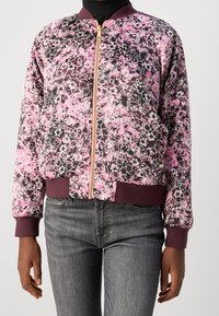 Colbert met kraag in een bloement patroon in roze en zwart, met ribgebreide manchetten en tailleband, een frontale rits en gouden hardware-details.