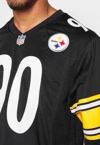 Maillot de la NFL noir avec de grands chiffres blancs, des accents rayés jaunes et noirs sur les manches, et un patch du logo des Steelers sur l'épaule.