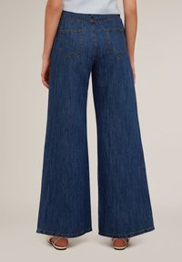 Pantaloni din denim cu picioare largi, în nuanță închisă, cu talie înaltă, două buzunare la spate și margini tivite pentru un finisaj curat.