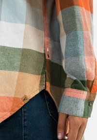 Chemise à carreaux aux nuances d'orange, vert, bleu et beige, en coton, avec poignets boutonnés et détail d'étiquette latérale.
