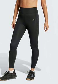 Mustat korkeavyötäröiset legginsit, jotka on valmistettu joustavasta materiaalista, ja joissa on sileä pinta sekä erottuva valkoinen logo vyötärön lähellä.