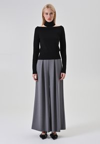 Top nero a spalle scoperte, abbinato a pantaloni grigi a vita alta e gamba larga. Le scarpe presentano un dettaglio a fiocco, creando una silhouette moderna.