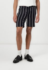 Navy striped shorts with a loose fit, featuring a drawstring waist and contrasting white stripes. Worn with black loafers and white socks.