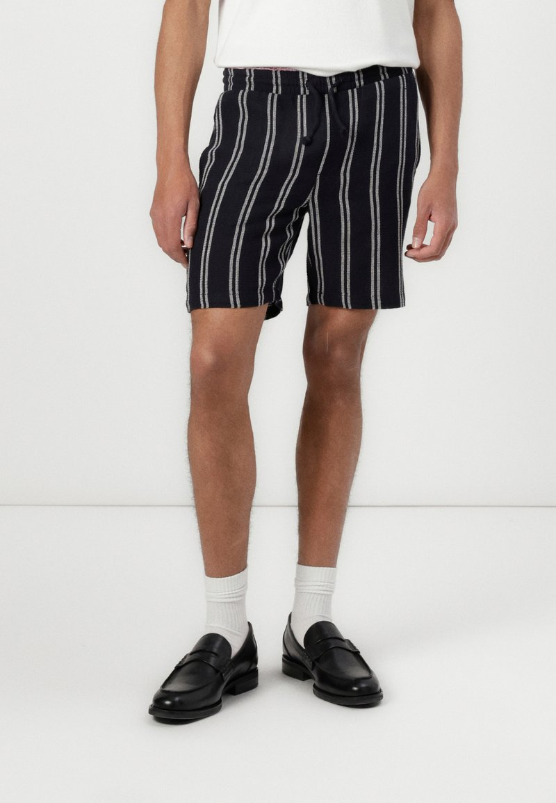 Navy striped shorts with a loose fit, featuring a drawstring waist and contrasting white stripes. Worn with black loafers and white socks.