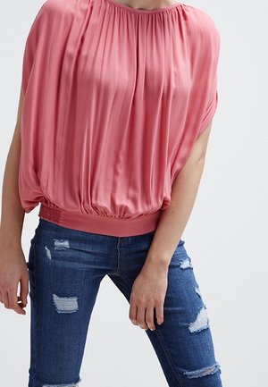 Pink, short-sleeve top with a gathered neckline and elasticized hem; paired with distressed blue jeans featuring frayed details.