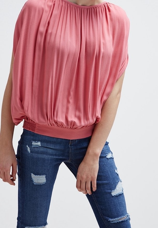 Różowa bluzka z krótkim rękawem, z marszczonym dekoltem i elastycznym dołem; w zestawie z podartymi niebieskimi dżinsami z postrzępionymi detalami.