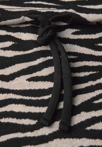 Tissu noir et beige à rayures avec un cordon de serrage noué à la taille. Texture lisse avec un motif animal audacieux.