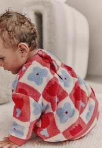 Pusero fleece, jossa on kirjallinen suunnittelu punaisten sydämien ja sinisten kukkien kuvioilla vaalean kermaisella taustalla. Vaatekappaleessa on punainen kaulus ja napit.
