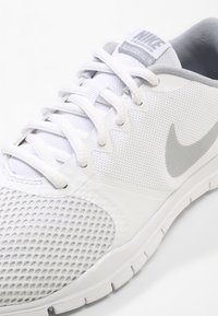 Hvid Nike træningssko med mesh-overdel, hvide snørebånd, lys grå swoosh-logo og polstret sål vist i vinkel nære udsigt.