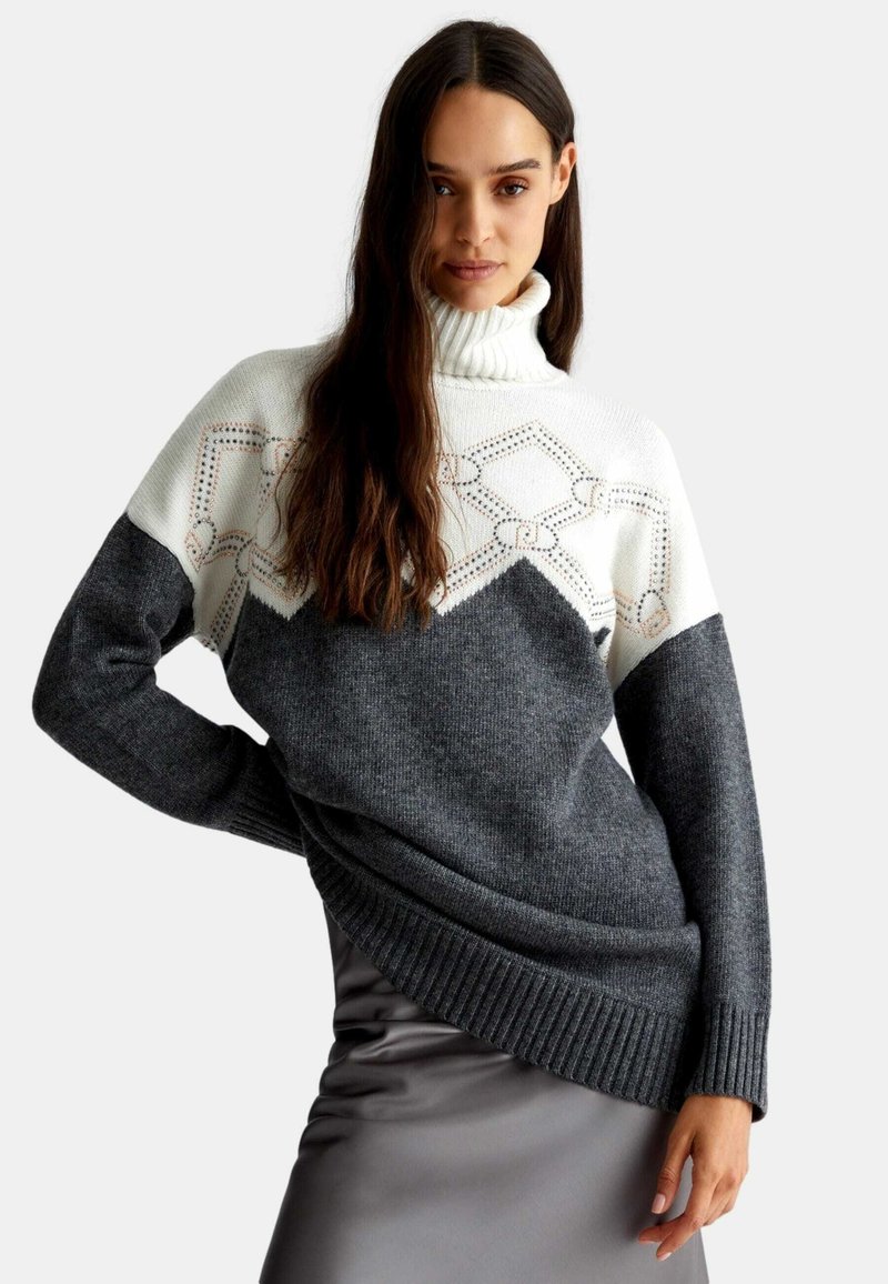 Maglione a maglia grossa con collo alto, parte superiore bianca con motivo geometrico e sezione inferiore grigio scuro. Orlo e polsini a costine.