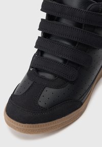 Mustad mustad sneakerid, mis on valmistatud perforatsiooniga nahast ja seemisnahast, elastsete rihmadega ning kummisest välispõhjast.