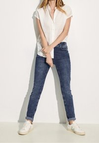 White short-sleeve button-up shirt paired with dark blue slim-fit jeans and white sneakers with green accents. Simple and casual outfit.