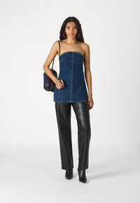 Denim-Trägertop ohne Träger mit einer Vordernaht, kombiniert mit einer schwarzen Kunstlederhose. Das Model hält eine schwarze Tasche und präsentiert einen eleganten, modernen Stil.