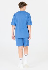 Blå kortærmet t-shirt og matchende shorts, lavet af blødt stof. Hvide sokker og sko fuldender outfittet. Designet er enkelt og afslappet.